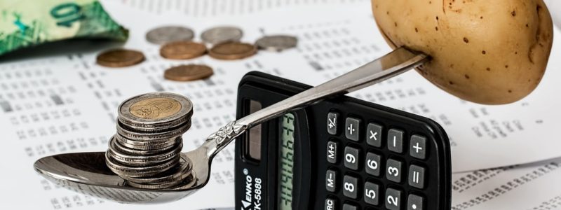 Haushaltsbuch führen – Löffel mit Münzen und Kartoffel auf Taschenrechner, umgeben von Rechnungen und Geld