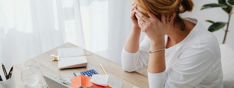 Frau am Schreibtisch mit Rechnungen und Taschenrechner – Symbolbild für „Schulden abbauen“