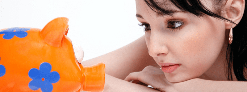 Sparen lernen – eine Frau blickt nachdenklich auf ein Sparschwein