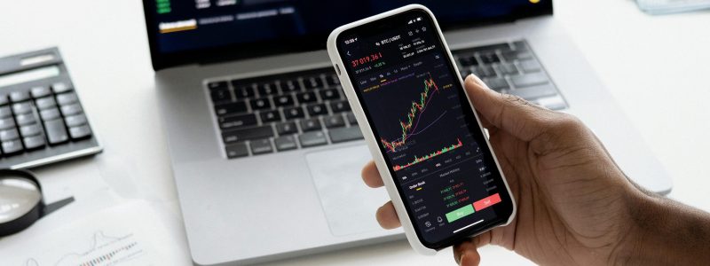 ETF-Sparplan einrichten – Smartphone mit Börsenkursen, im Hintergrund Laptop, Taschenrechner und Papiere