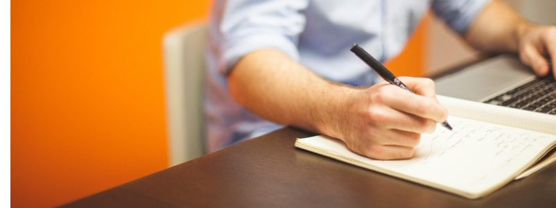 Mann schreibt ins Notizbuch – finanziell bei Null anfangen