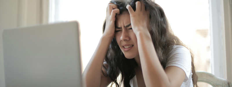 Frau hält sich frustriert die Haare vor einem Laptop – Symbol für das Gefühl, nie reich zu werden